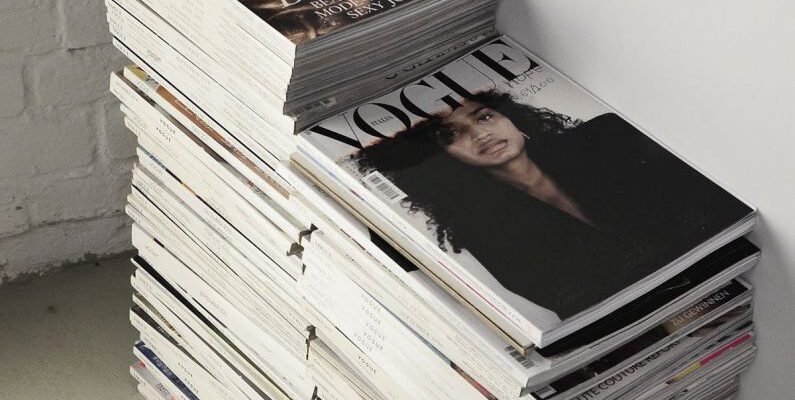 Self-Publishing - High angle many fashion magazines stacked on floor against white brick wall in studio