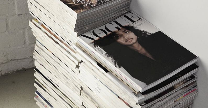 Self-Publishing - High angle many fashion magazines stacked on floor against white brick wall in studio